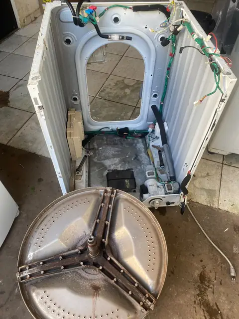 Máquina de lavar desmontada com cesto sobre o piso da oficina
